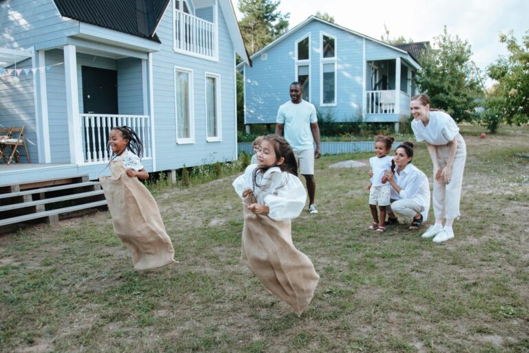 Group of children enjoying a sack race in a backyard setting, surrounded by family.
