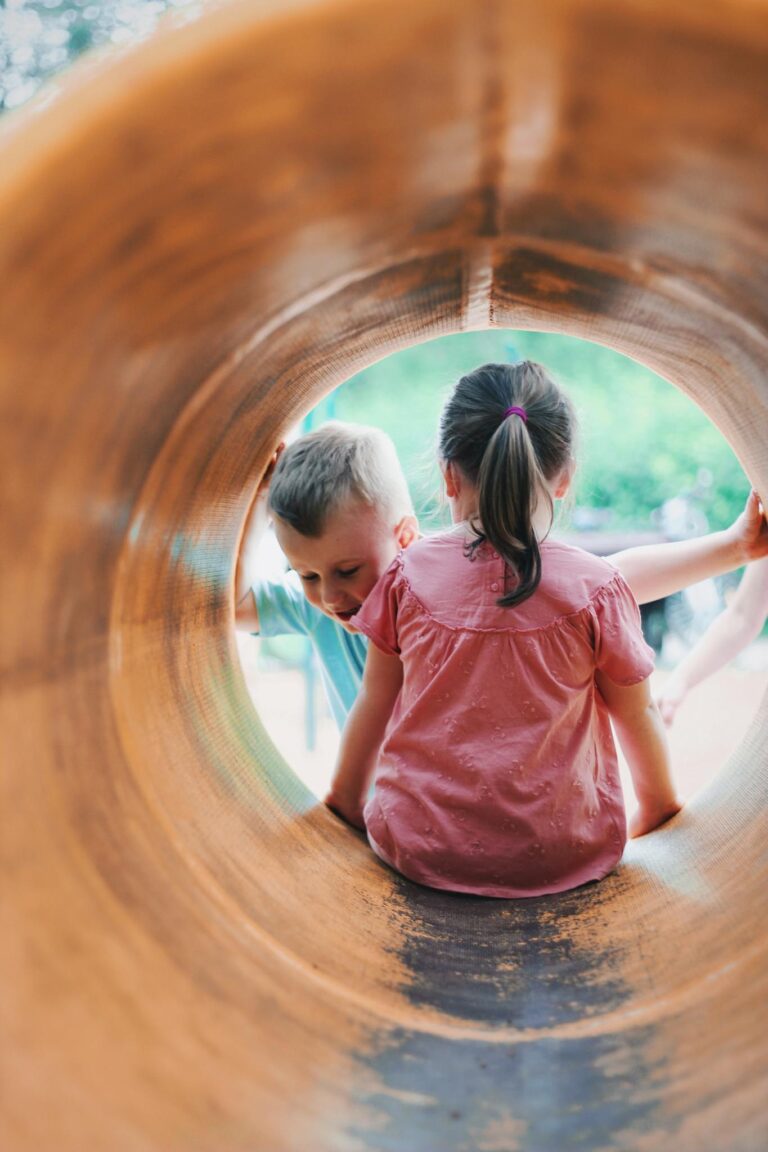 Two children enjoying playtime inside a playground tube on a sunny day.